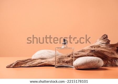 Transparent perfume bottle near the aged weathered wooden snag and stones. Perfume with woody notes concept. Background with copy space. Royalty-Free Stock Photo #2215178101