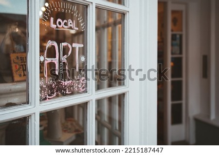 Local small business window display with lettering advertising local art. Entrance is empty and white window frames show many layers of paint. Tourist town local shop selling art.