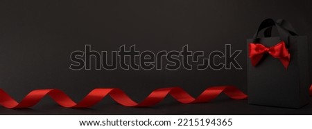 Gift in black paper bag with red ribbon on black background, design banner black friday sale concept copy space for text