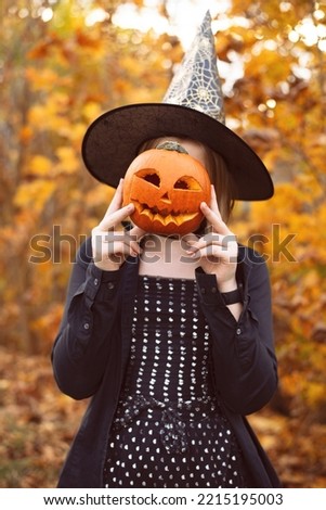 A teenage girl with a pumpkin for Halloween in a black witch hat. Teen girl having fun celebrating Halloween concept in the woods