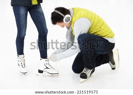 A picture of a young man tying his friend's skates on a skating rink