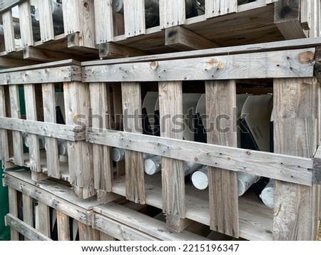 Wooden boxes with materials and pipes are stored in a warehouse with industrial equipment.