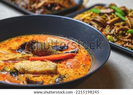 tom yum - spicy thai soup with chicken in a black bowl on the table, top view.
