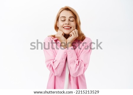 Portrait of smiling romantic girl daydreaming, close eyes and dreaming, fantasizing, standing over white background