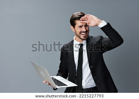 Man with beard brunette business with headache looking at laptop screen on hands on gray background in business suit. Work online business