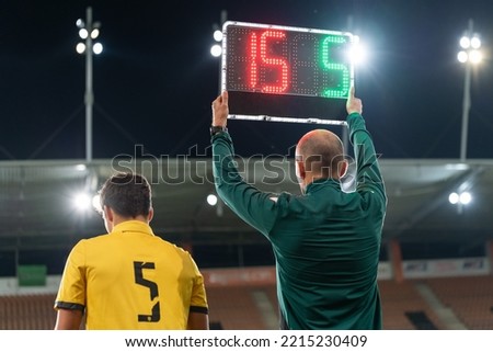 Sideline referee shows players substitution during football match. Royalty-Free Stock Photo #2215230409