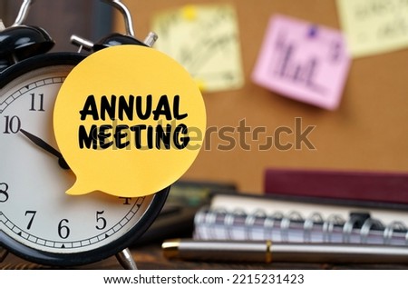 Business concept. The alarm clocks have a sticker with the inscription - ANNUAL MEETING. There are office items in the background in a blurry background. Royalty-Free Stock Photo #2215231423