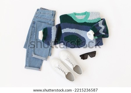 Blue jeans, blue knitted sweater, white sneakers and sunglasses lying on white background. Overhead view of women's casual outfit. Trendy stylish women clothes. Flat lay, top view. Royalty-Free Stock Photo #2215236587