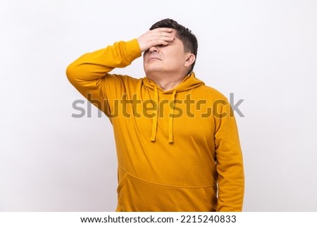 Don't want to look at this. Portrait of middle aged man covers eyes, disgust from something shameful, scared afraid to see, wearing urban style hoodie. Indoor studio shot isolated on white background. Royalty-Free Stock Photo #2215240833