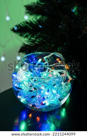 A glass jar filled with glowing garland placed on a table in a dark room, blurred lights, soft focus, festive mood