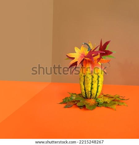 Creative Halloween design made of yellow pumpkin with autumn leaves crown surrounded by colorful leaves against gold and orange background. Minimal concept. Copy space. Autumn art.