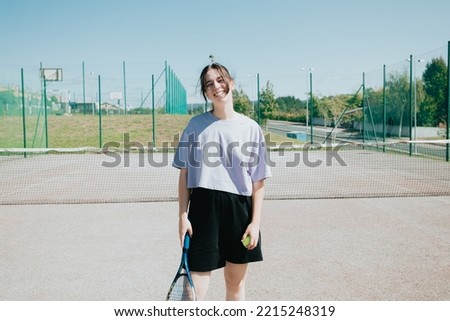 Frontal portrait of a tennis woman player at the court smiling cheerful to camera, learning sports
