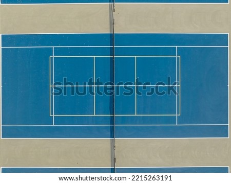 Aerial photo of outdoor blue tennis courts with yellow pickleball lines and gray out of bounds area.	