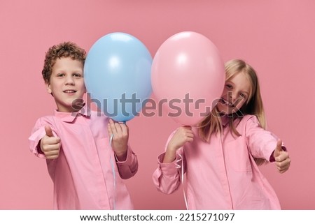 funny children, a boy and a girl are standing in pink clothes on a pink background and playing with inflatable balls. In the hands of the girl is pink, and the boy has blue balloons