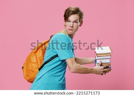 funny, guy student cheerfully holds books in his hands while standing in T-shirt and with a backpack on his back. Studio photo on a pink background, the concept of preparing for the school season