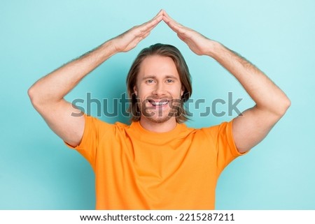 Photo of funny pretty man wear orange t-shirt smiling showing arms roof isolated turquoise color background Royalty-Free Stock Photo #2215287211