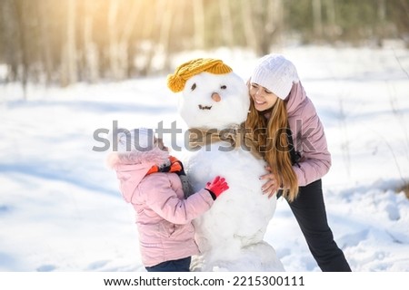 The family plays in the winter forest and makes a snowman. Mom and daughter are playing near the snowman.