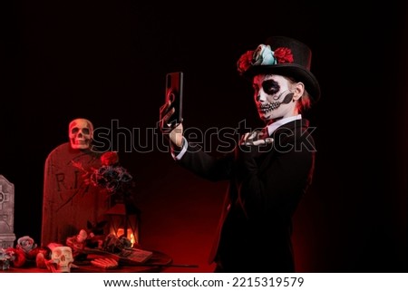 Santa muerte taking pictures on mobile phone, wearing dios de los muertos halloween costume and make up. Woman capturing image being dressed as la cavalera catrina over black background.