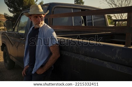 Portrait of adult man in cowboy hat standing against a vintage truck during sunset