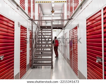 Man in a self storage facility with red metal doors. Keeping your personal staff safe concept. Royalty-Free Stock Photo #2215341673