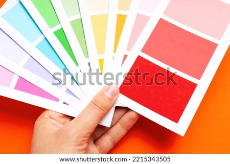 Female hand holding color palettes on orange background