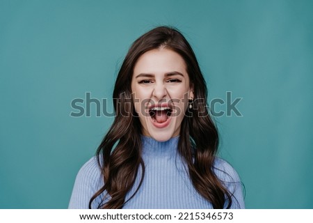 Close up of screaming young woman in lilac sweater with loose wavy hair over turquoise studio background. Pretty hispanic girl at studio calling people to come. Mockup, stock, promo, discount.