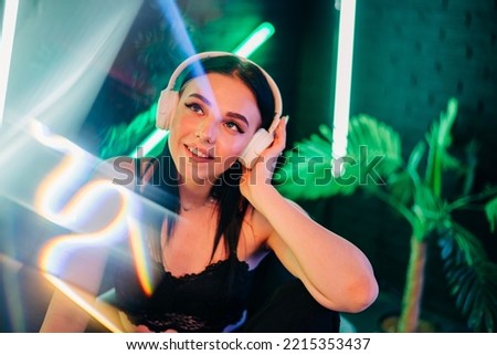 Fashion pretty woman with headphones listening to music over neon background at studio. Royalty-Free Stock Photo #2215353437
