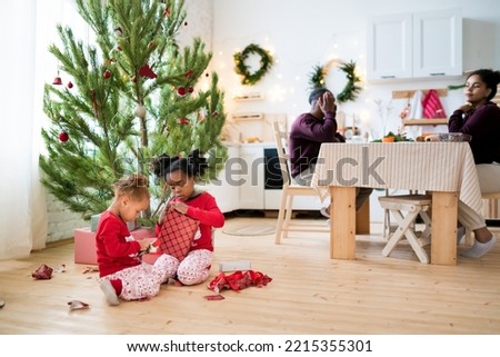 Children unpacking Christmas gifts. Two African American girls in Xmas pajamas sitting on the floor near the christmas tree and opening Christmas presents on morning. Selective focus