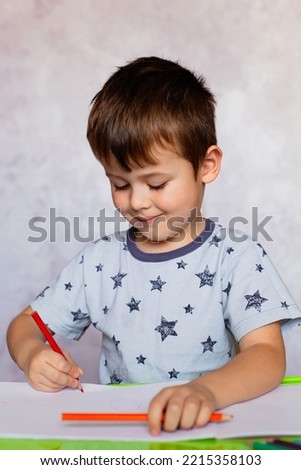Little boy drawing with color pencils. Boy, drawing a picture for fathers day. Small boy draws at the table. Little boy is holding color pencils.