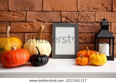 Blank frame with Halloween pumpkins and lantern on mantelpiece near brick wall