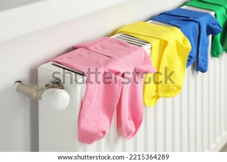 Different colorful socks hanging on white radiator indoors