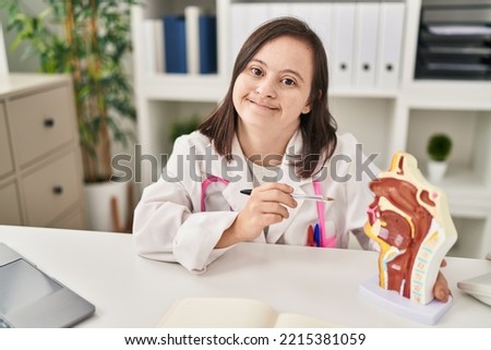 Down syndrome woman wearing doctor uniform pointing to anatomical model of respiratory system at clinic