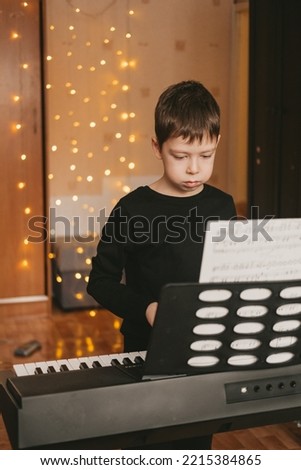 a boy in a black T-shirt plays the piano, against the background of a Christmas garland