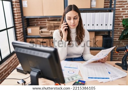 Young beautiful hispanic woman ecommerce business worker talking on smartphone reading document at office