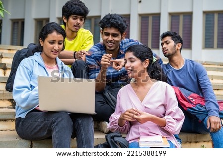 Group of happy students checking results on laptop while sitting on college campus - concept of education, technology and project work discussion.