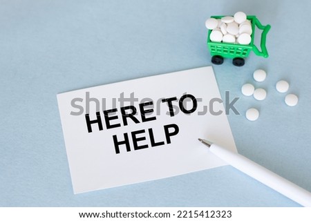 The text WE ARE HERE TO HELP on a card on a blue background next to a pen and pills
