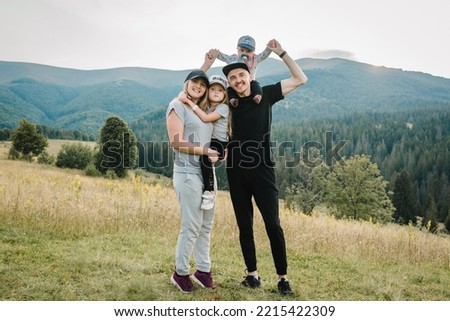 Portrait of happy young family spending time together in field. Mom, dad holds baby son and daughter stand on grass in mountains. The concept of family holiday. Mother, father hug kids on autumn day.
