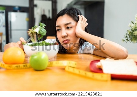 Unhappy female looking to organic greens vegetable salad in weight loss diet and wellness on table. Tired woman dislike eat bored with food healthy salad breakfast in kitchen. Diet food concept.