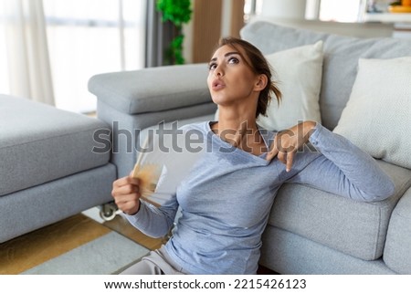 Stressed annoyed woman using waving fan suffer from overheating, summer heat health hormone problem, no air conditioner at home sit on sofa feel exhaustion dehydration heatstroke concept