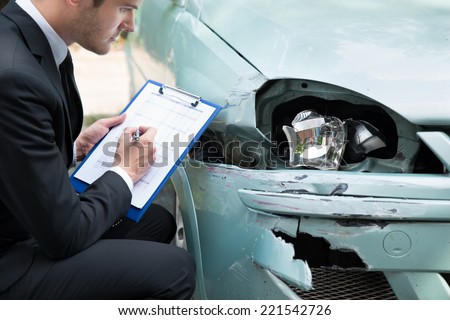 Side view of writing on clipboard while insurance agent examining car after accident Royalty-Free Stock Photo #221542726