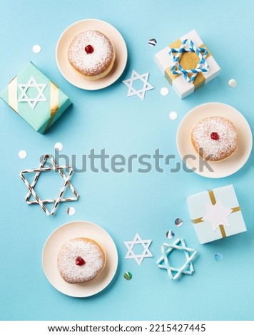 Hanukkah sweet doughnut sufganiyot with powdered sugar and fruit jam, gift boxes on blue paper background. Jewish holiday Hanukkah concept. Top view, copy space.
