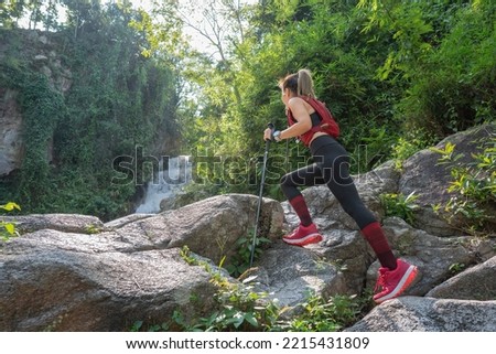 Young fitness woman running at forest trail on waterfall background