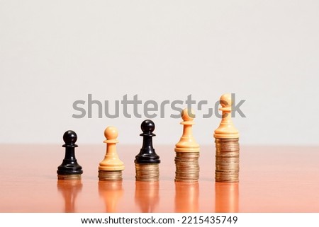 Black and white chess pawns on coins stacked on a wooden table with white background. Concept of personal success, entrepreneurship and business development.