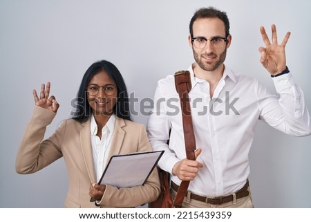 Interracial business couple wearing glasses smiling positive doing ok sign with hand and fingers. successful expression. 