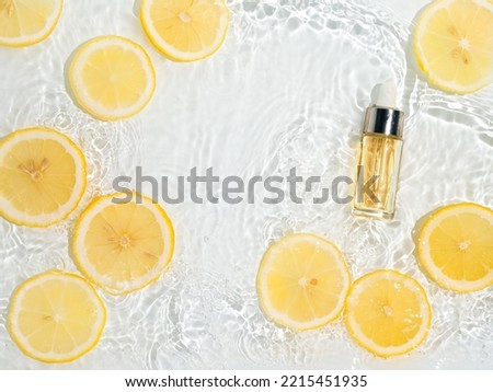 Luxury cosmetic peeling or serum in glass bottle with pipette in clean transparent water with lemon slices over clear water background. Water splashing on water surface in sunlight. flatlay copy space Royalty-Free Stock Photo #2215451935