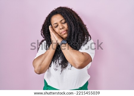 Plus size hispanic woman standing over pink background sleeping tired dreaming and posing with hands together while smiling with closed eyes. 
