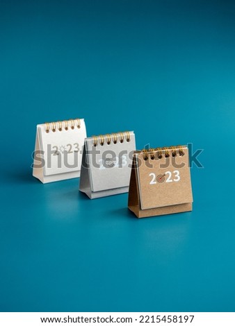 Business action plan with goal, management and idea icon signs on small beige, grey and white desk calendar year 2023 on blue background, vertical style. Three step of strategy concept, minimal style.