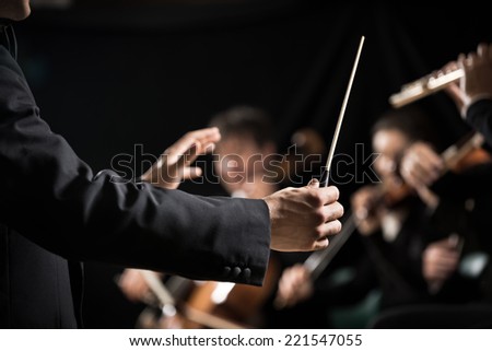 Conductor directing symphony orchestra with performers on background, hands close-up. Royalty-Free Stock Photo #221547055