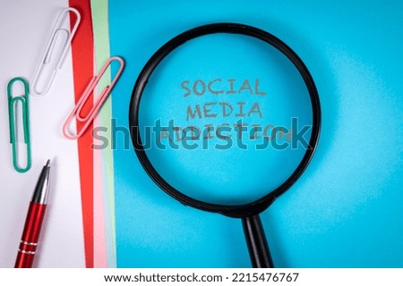 Social media addiction. Text and magnifying glass on blue paper background.