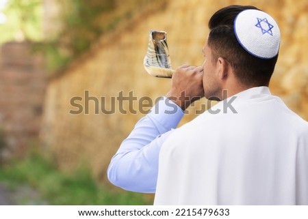 Jewish man in kippah and tallit blowing shofar outdoors. Rosh Hashanah celebration Royalty-Free Stock Photo #2215479633